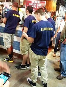 A group of young men all wearing identical Be Different t-shirts standing in a queue together