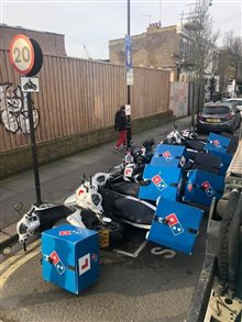 A row of Dominos delivery mopeds that have fallen over like dominoes on a London street