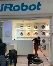An employee manually mopping the floor of an iRobot store surrounded by robotic vacuum cleaners on display